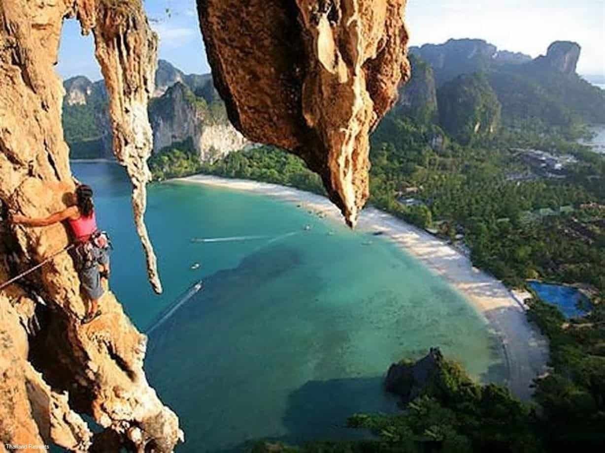 Rock climber high on the limestone cliffs at Railay in Krabi looking down at the sea, Thailand